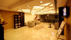 A hotel lobby with a high ceiling, recessed lighting, a reception desk, seating area, and a television screen. - Hotel The Class (New Delhi)