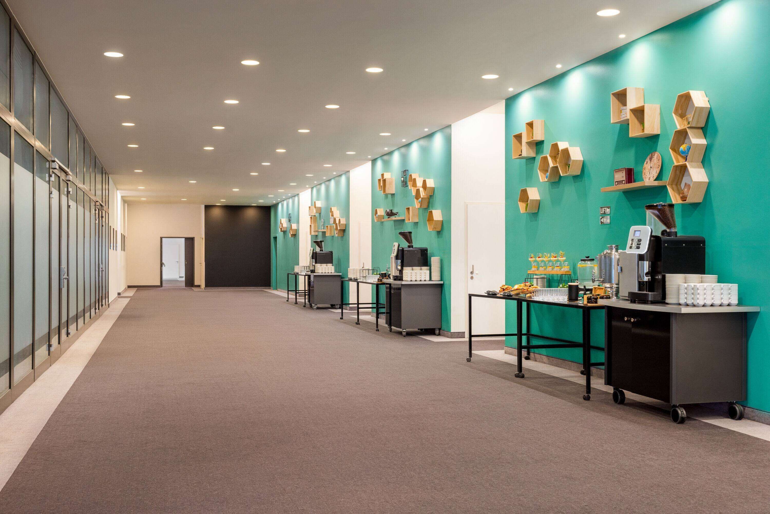 A modern hotel corridor with teal walls, wooden wall decor, and a coffee station.