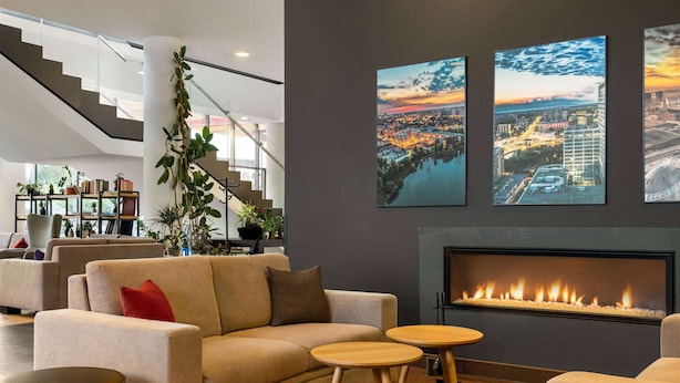 Un salon moderne comprenant un canapé, deux petites tables rondes, une cheminée et trois tableaux représentant des paysages urbains accrochés au mur.