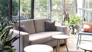 Un salon moderne avec un canapé beige, deux tables rondes et diverses plantes en pot.