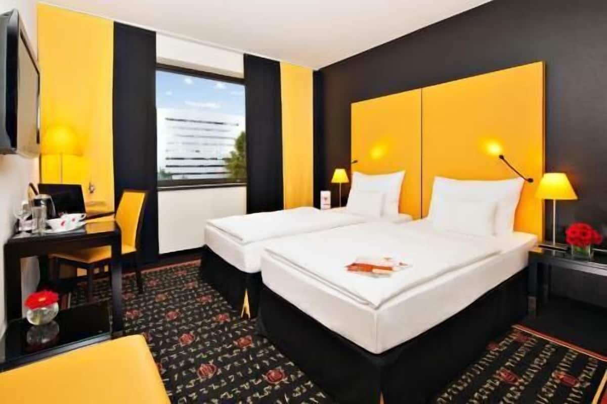 Habitación de hotel con una cama grande, un escritorio, una silla, un televisor y una ventana con vista a un edificio.