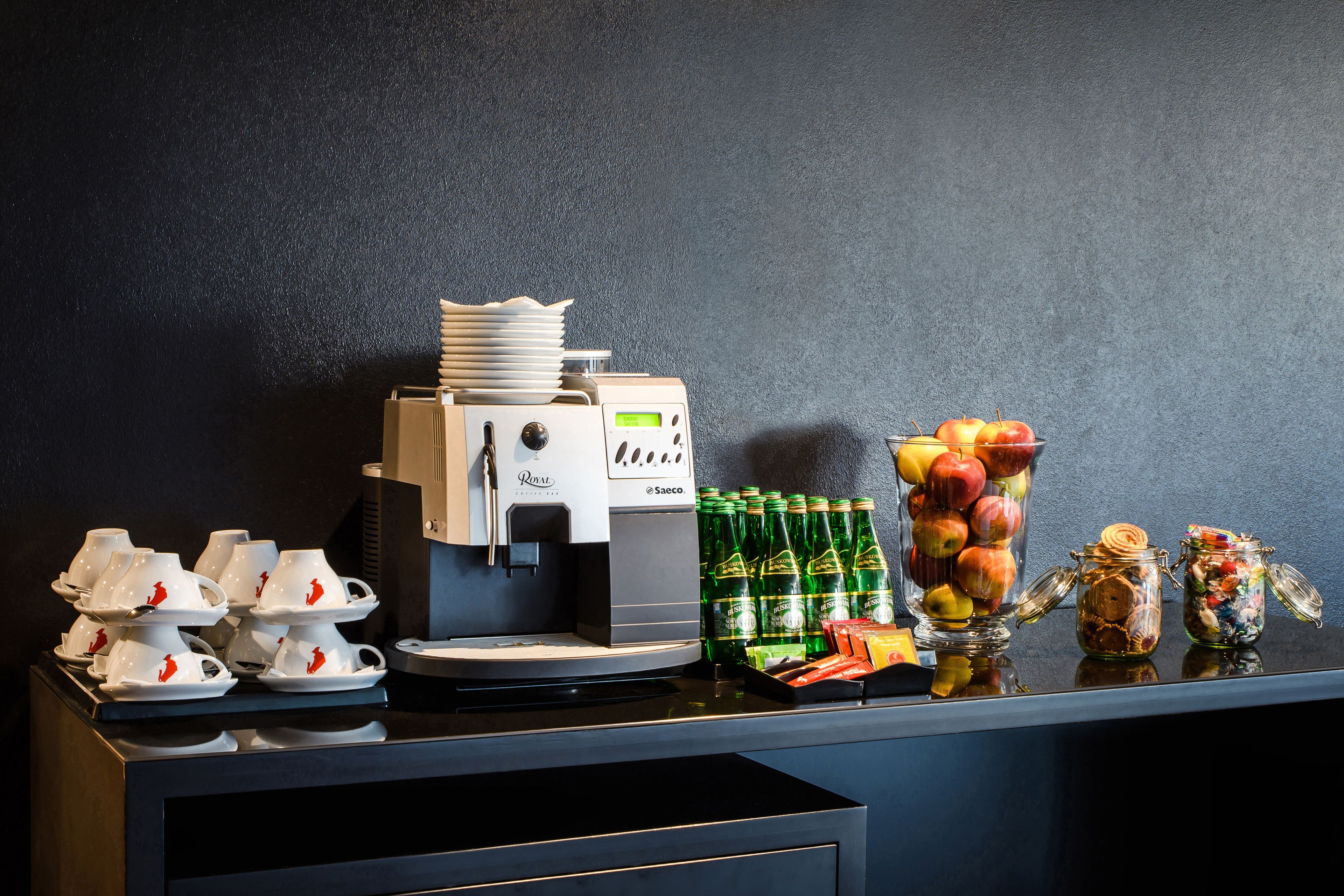 Uma estação de café com máquina de café, xícaras e uma seleção de frutas.