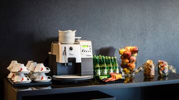 Uma estação de café com máquina de café, xícaras e uma seleção de frutas.