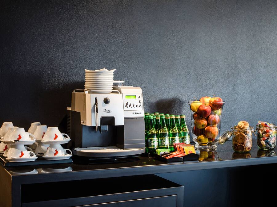 Uma estação de café com máquina de café, xícaras e uma seleção de frutas.