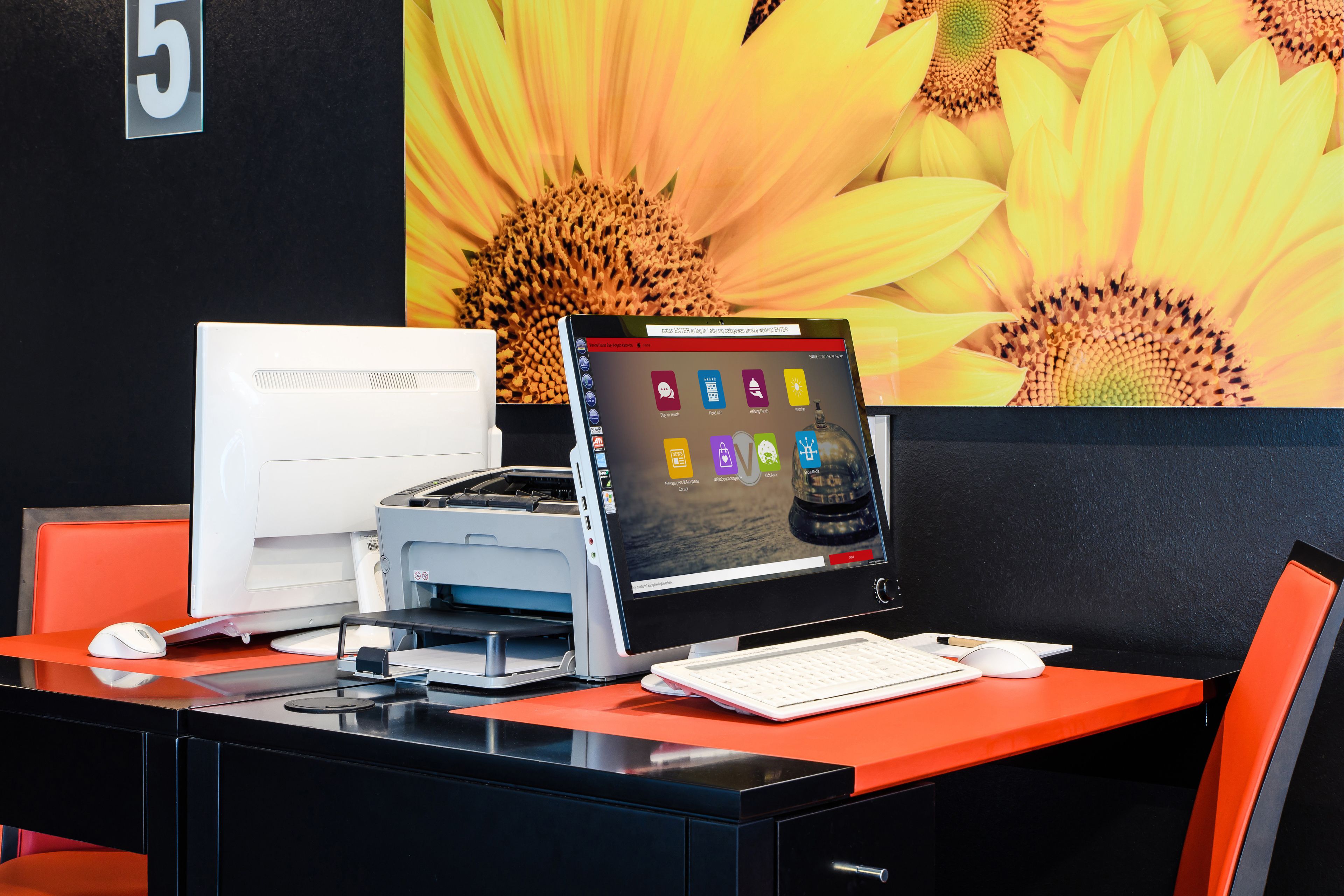 Un escritorio con una computadora, una impresora y un gran mural floral de fondo.