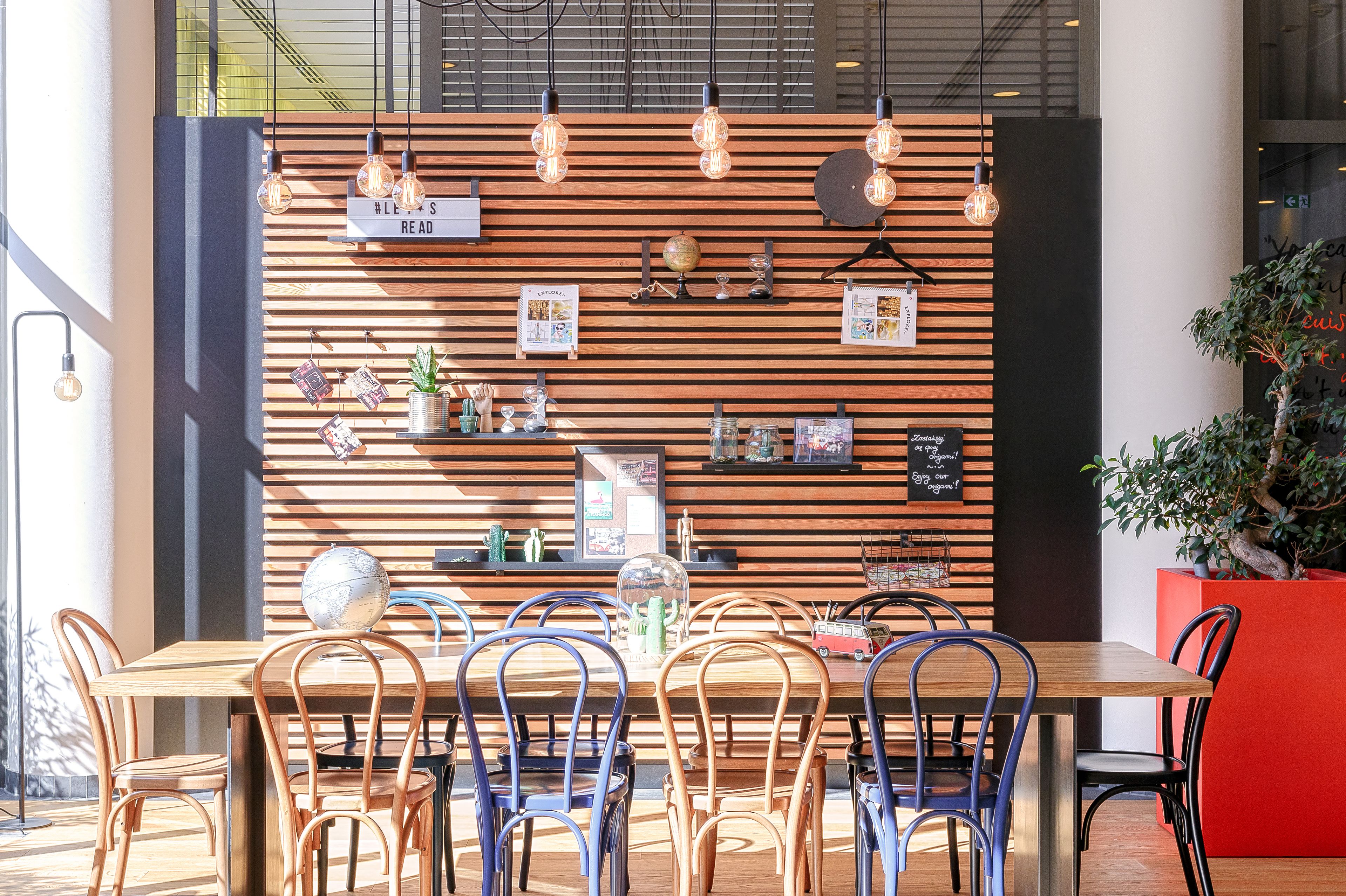 A modern dining area with a wooden slatted wall, hanging light bulbs, and a variety of decorative items.