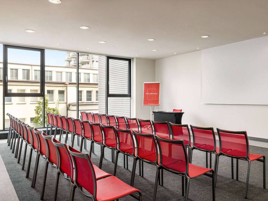 Un salón de conferencias con filas de sillas rojas, una pantalla de proyector y un atril.