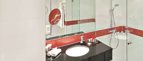 A modern bathroom with a glass shower enclosure, a white sink with a black countertop, and red-tiled accents.