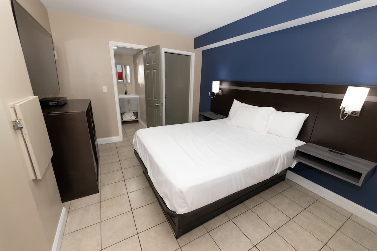 Habitación de hotel con cama, mesitas de noche, armario y baño visible a través de una puerta abierta.