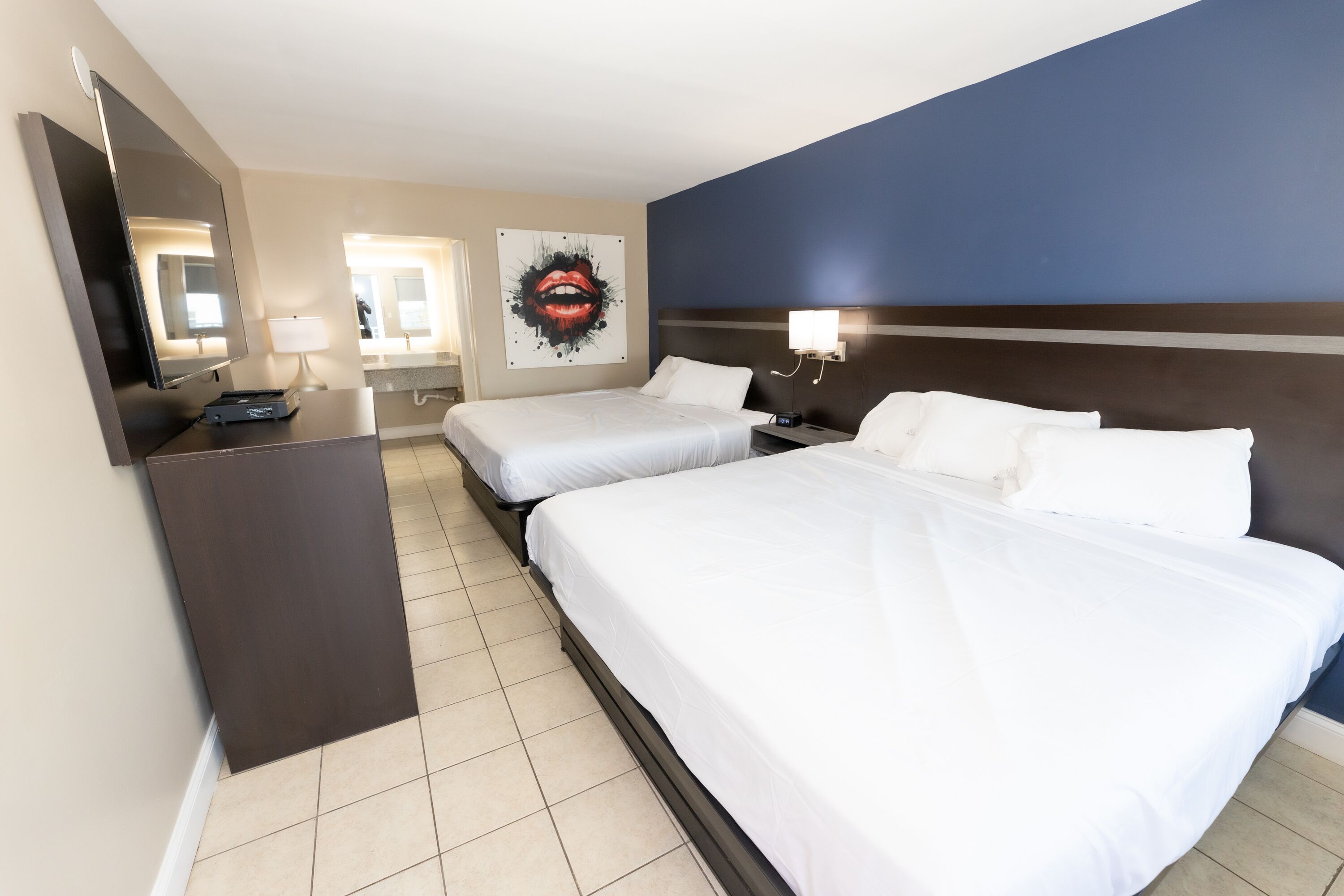 Une chambre d’hôtel avec deux lits, un téléviseur à écran plat, un bureau avec une lampe et une œuvre d’art accrochée au mur.