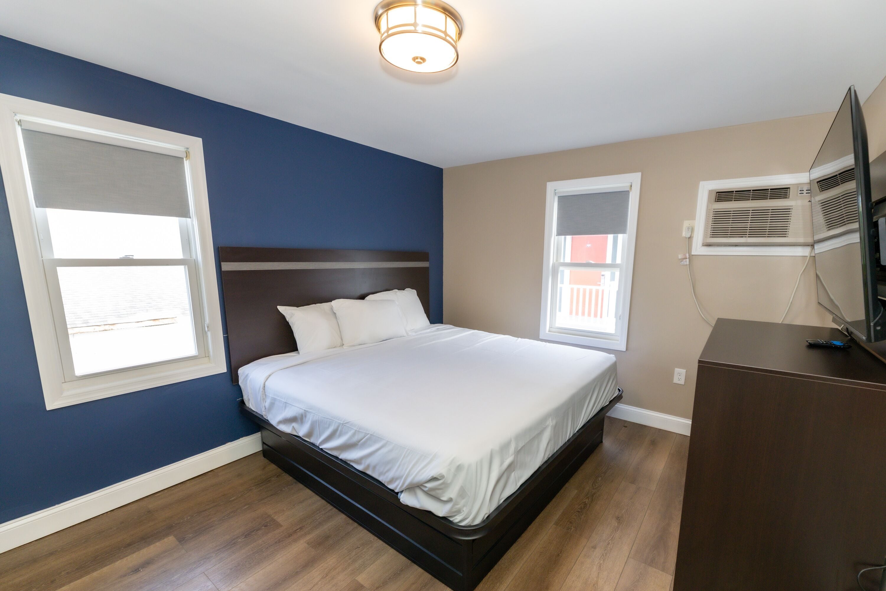 A bedroom with a bed, a dresser, and two windows.