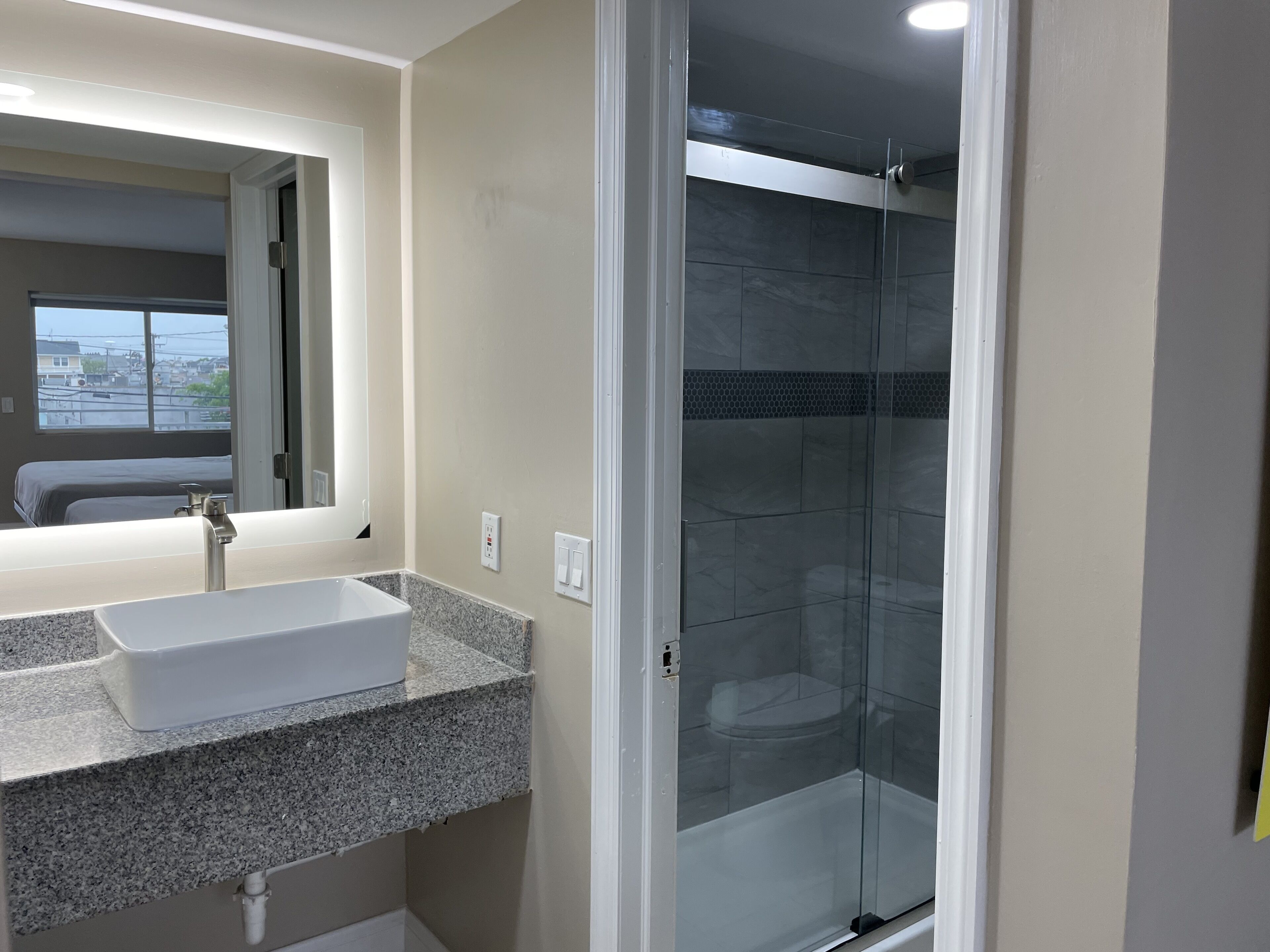 A bathroom with a granite countertop sink, a mirror, and a glass-enclosed shower.
