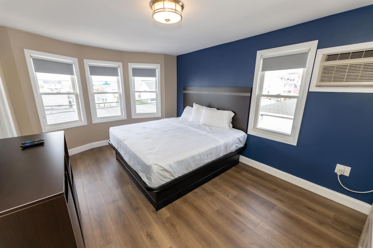 Un dormitorio con una cama, un aparador y tres ventanas.