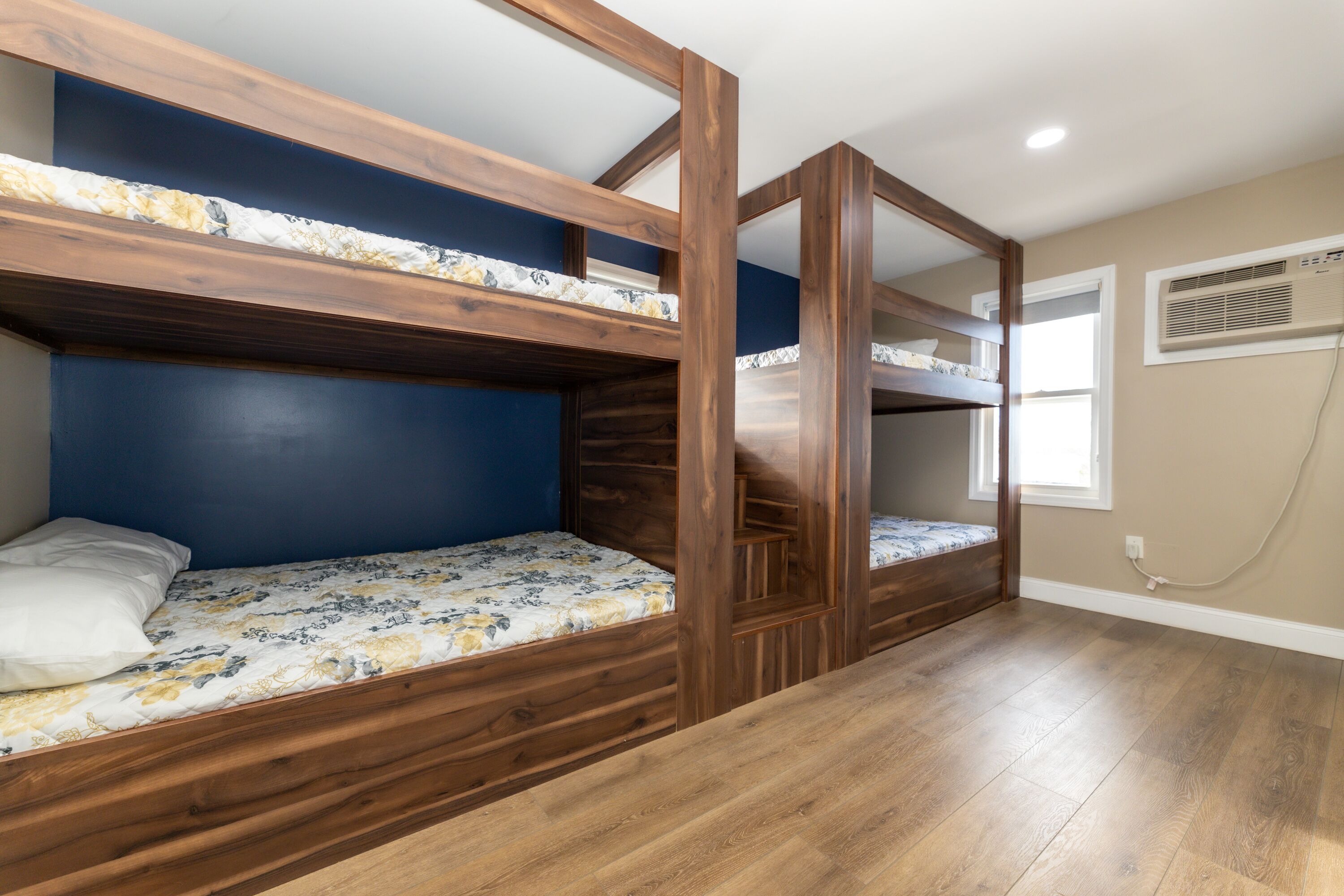 Habitación con literas de madera, una ventana con persianas y un aire acondicionado instalado en la pared.