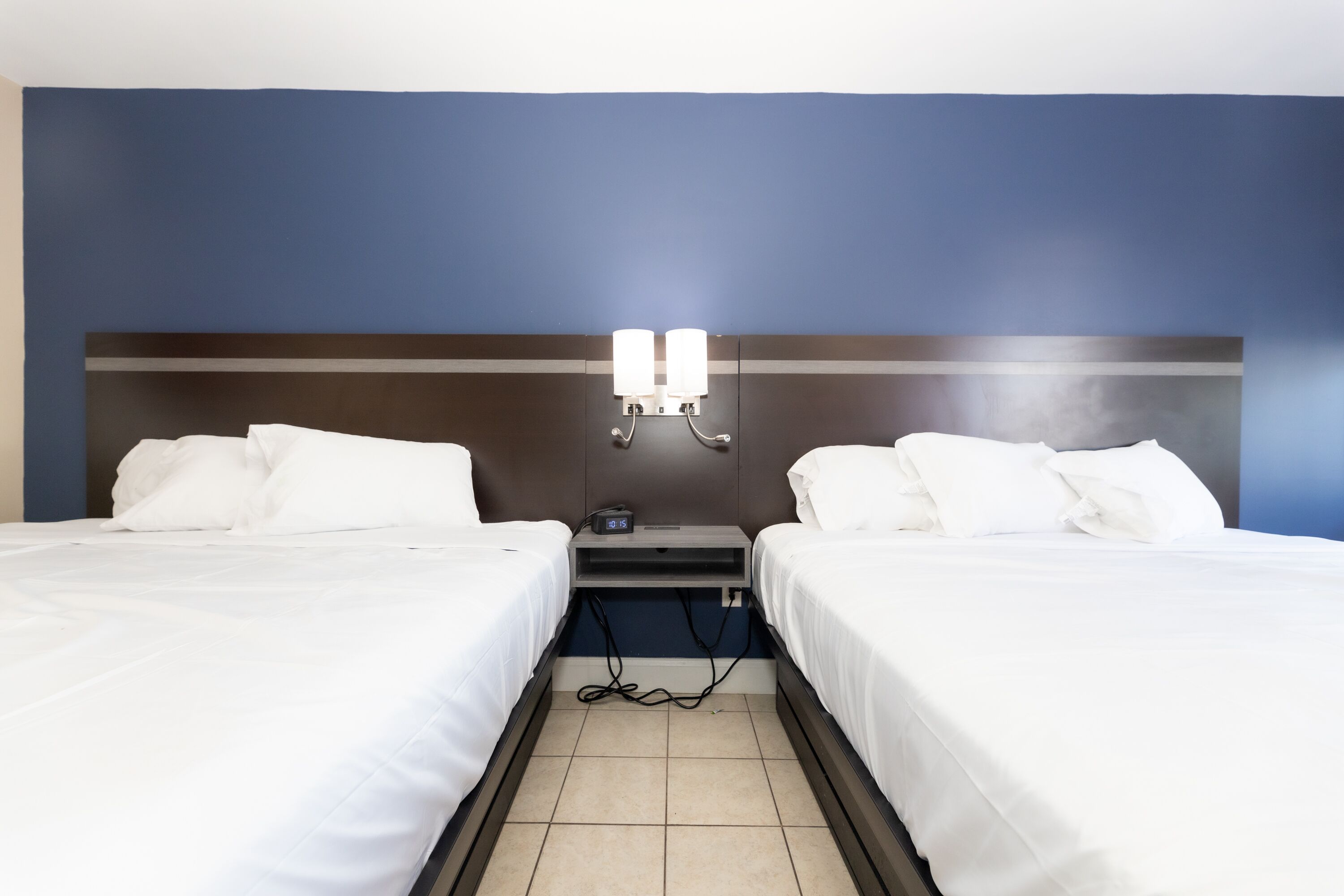 Une chambre d’hôtel avec deux lits, une table de chevet avec une horloge et un luminaire fixé au mur.