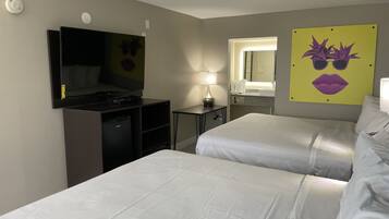 Habitación de hotel con dos camas, televisión, escritorio, lámpara, espejo y baño con lavabo y espejo.