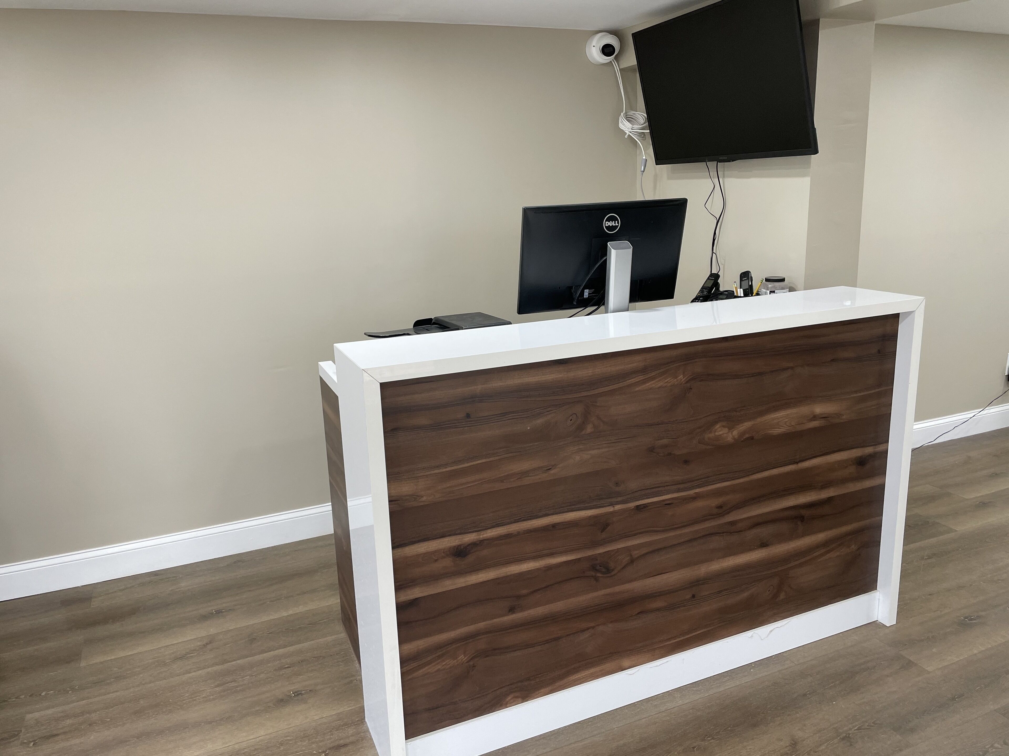 Ein Empfangstresen mit Holzoptik und weißer Verzierung, ein Flachbildschirm und eine an der Wand befestigte Überwachungskamera.
