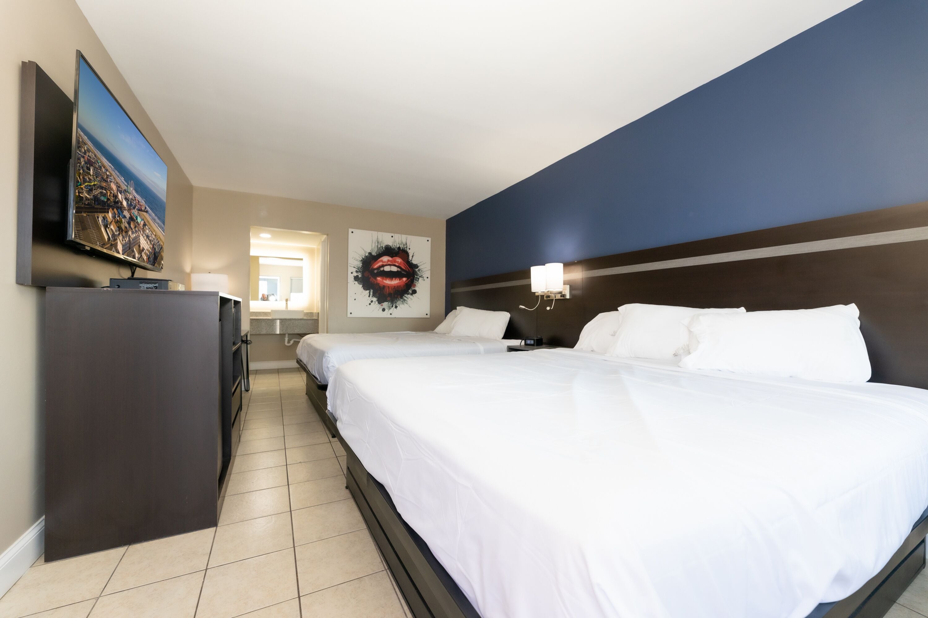 A hotel room with two beds, a flat-screen TV, a painting, and a nightstand with a lamp.
