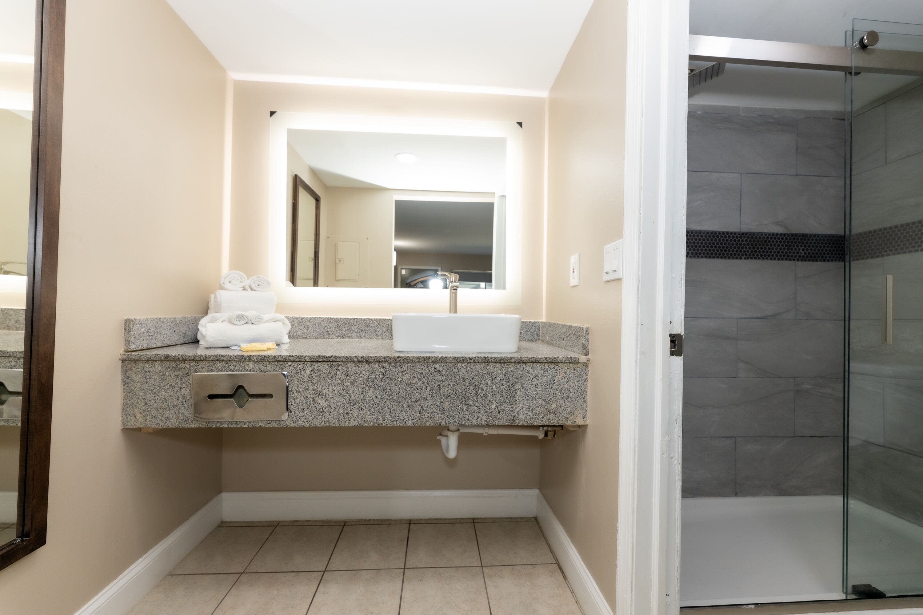A bathroom with a granite countertop, a white sink, a mirror, and a glass shower enclosure.