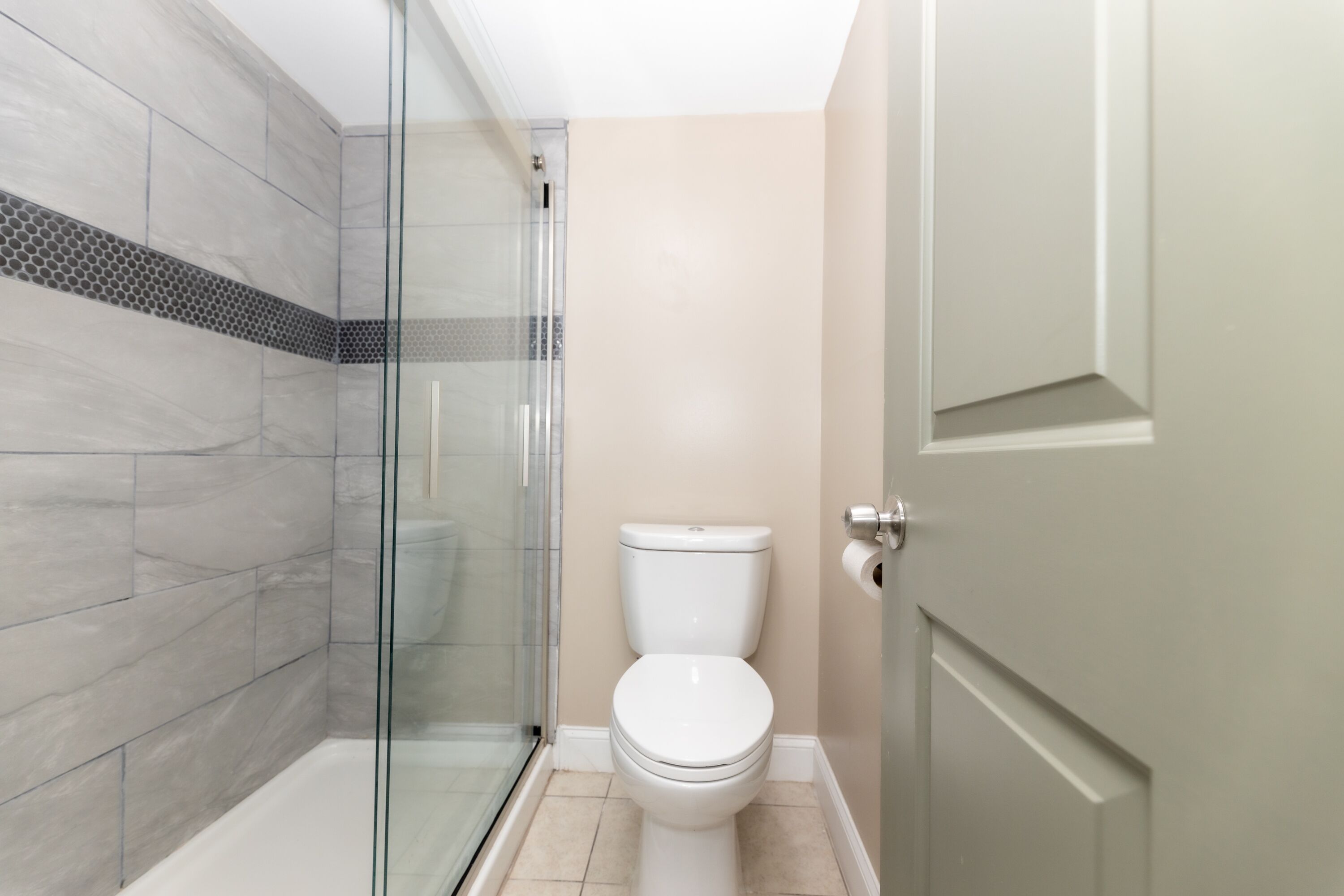 A bathroom with a glass-enclosed shower, a toilet, and a door.