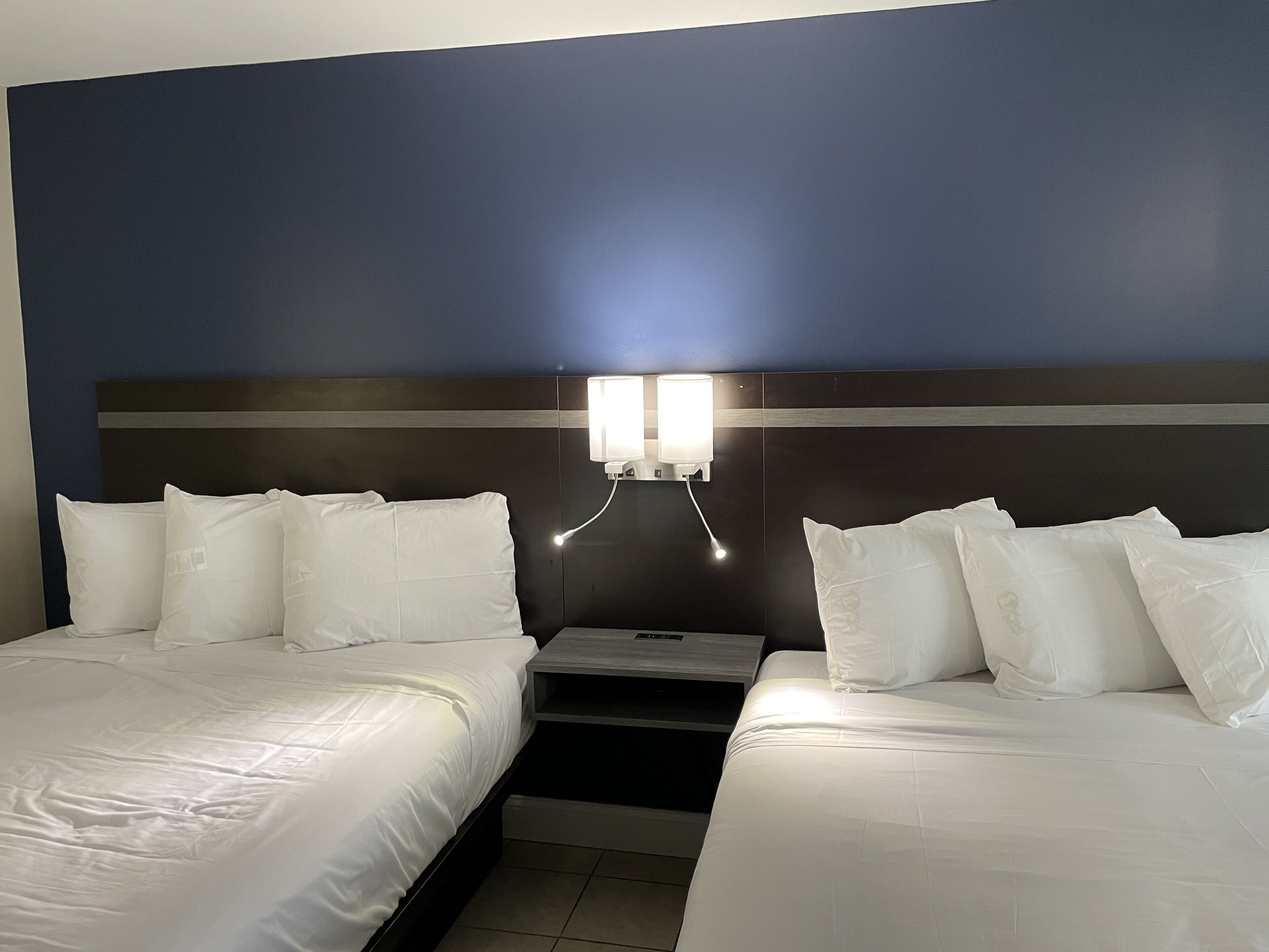 A hotel room with two beds, a nightstand, and a wall-mounted light fixture.