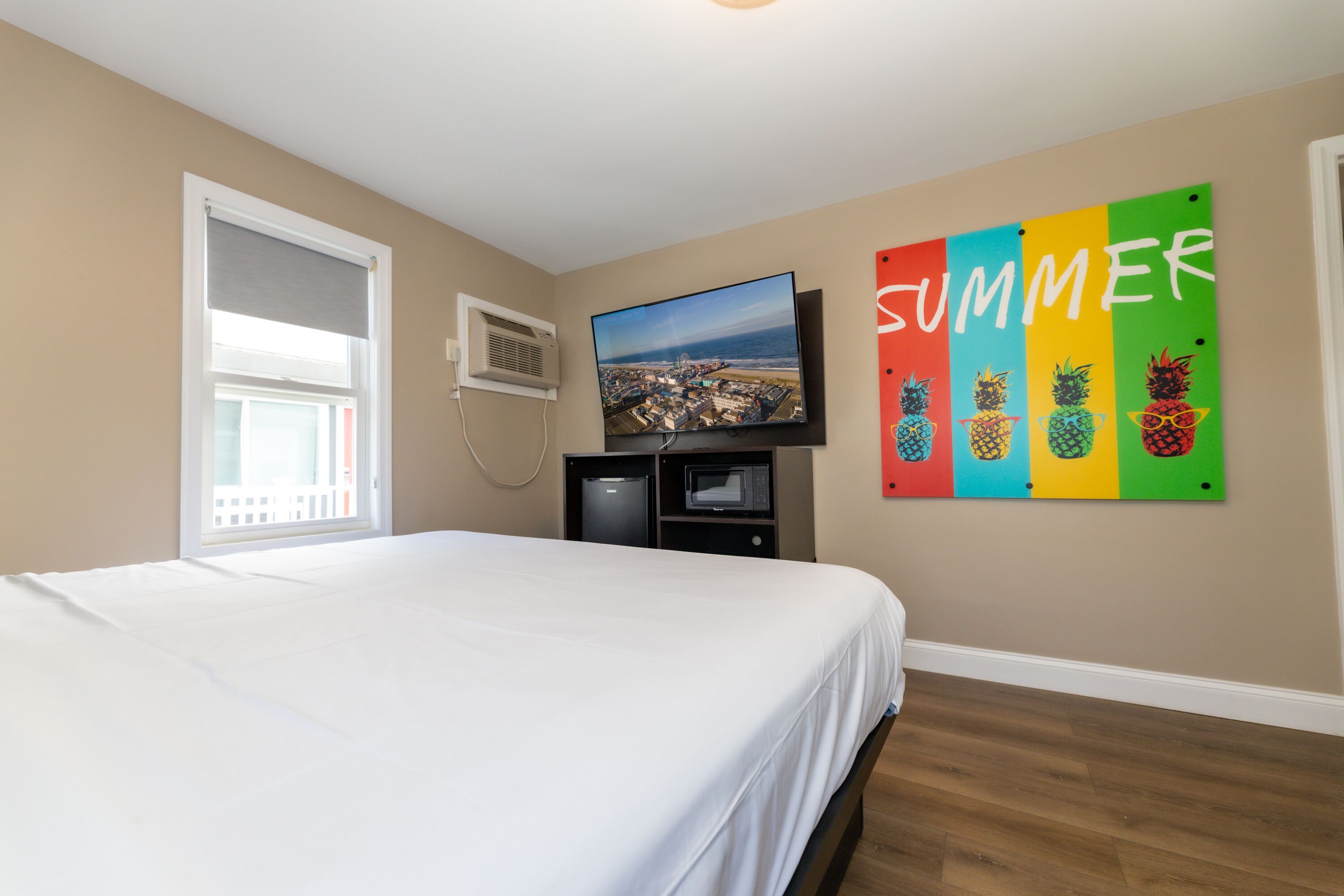 Un dormitorio con cama, televisor, ventana y una pared con un cartel que dice 'SUMMER'.