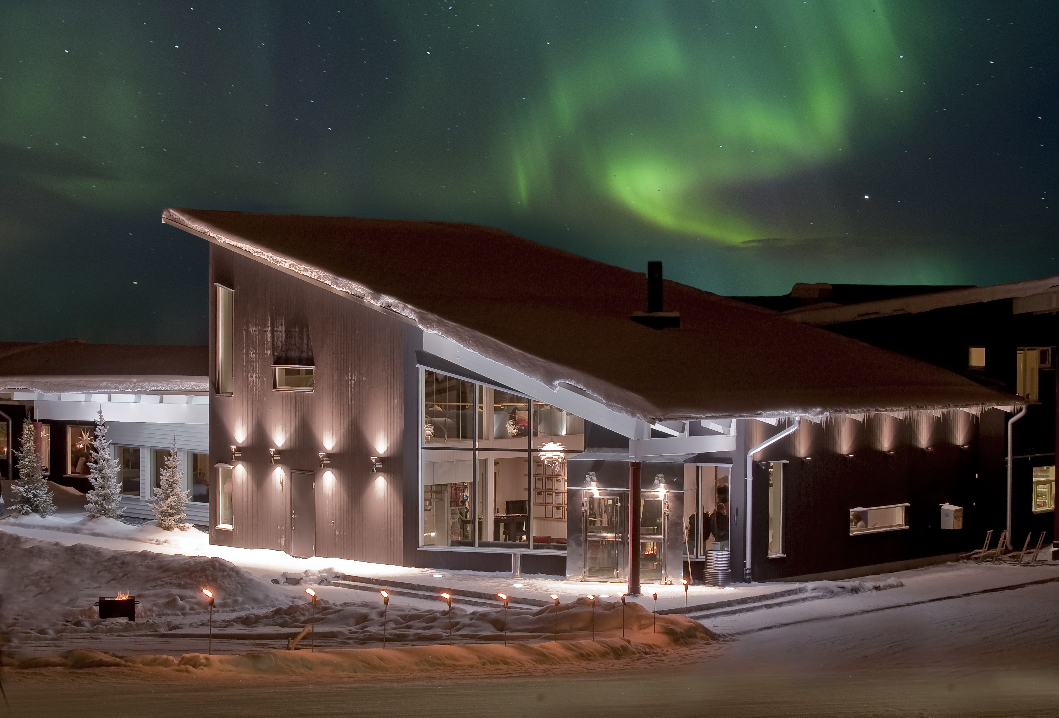 Una casa moderna con ventanas amplias y un porche cubierto, rodeada de nieve.