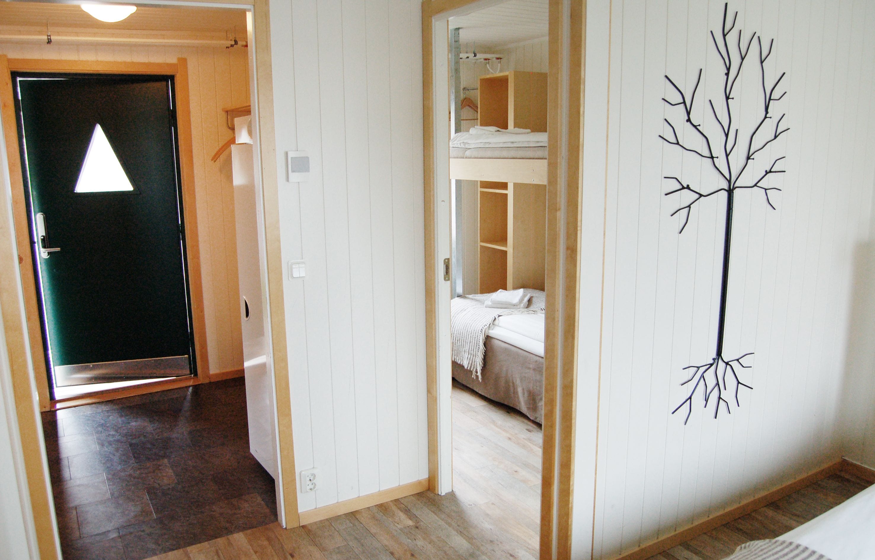 A room with a bunk bed, a door with a triangular light, and a wall-mounted tree decoration.
