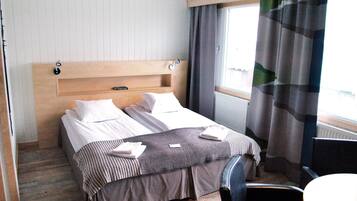 A hotel room with a wooden headboard, two beds, a small table, and a window with curtains.