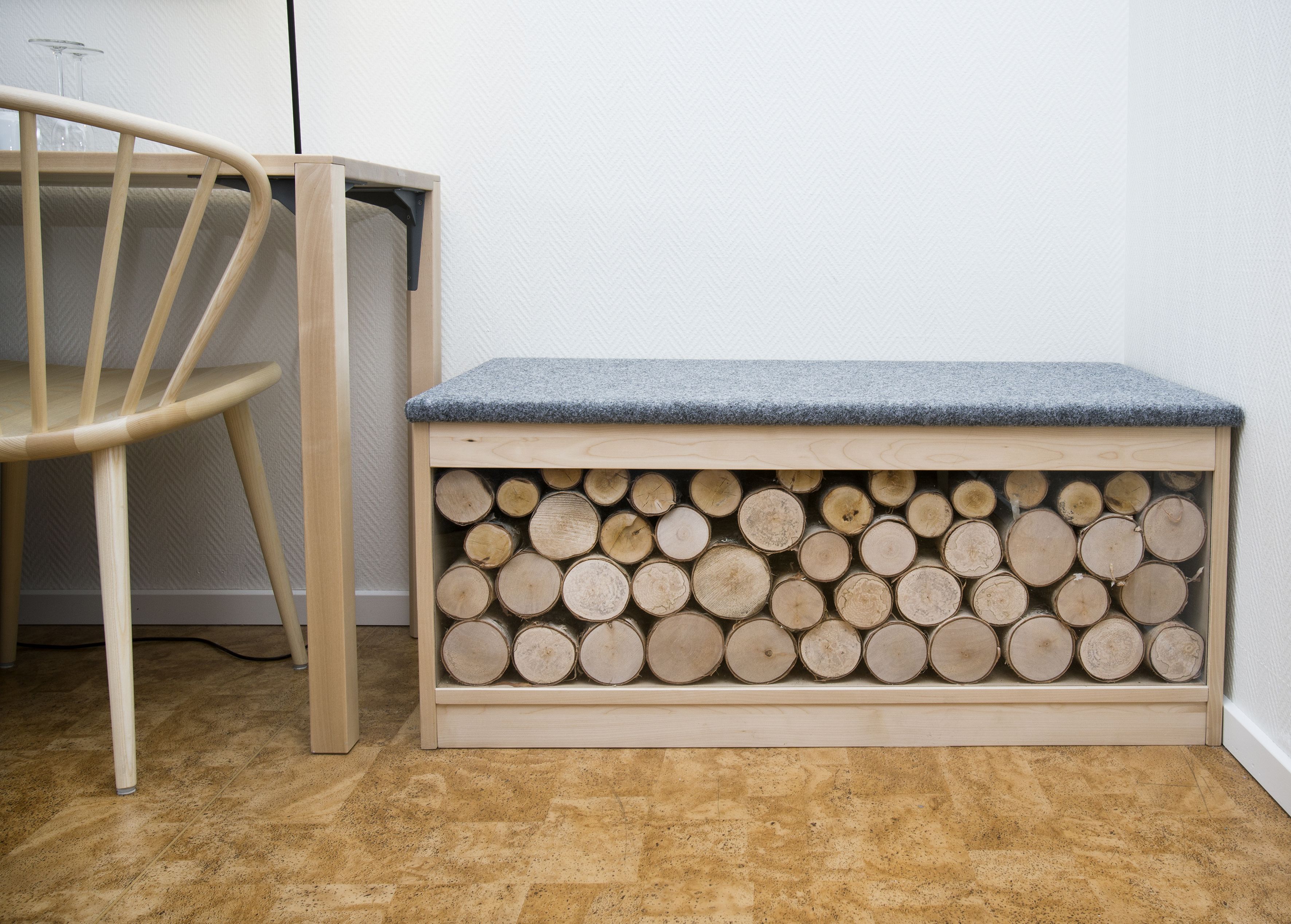 Un banco de madera con tapa gris y un compartimento lleno de leña.