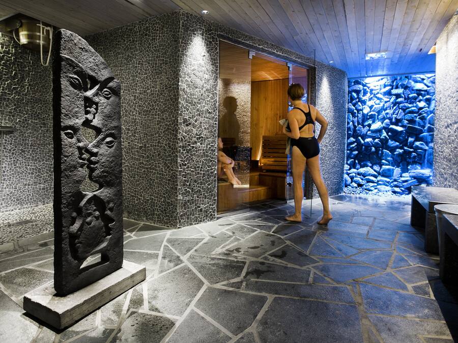 Un área de spa con paredes de piedra, suelo de mosaicos, un banco de madera y una escultura de piedra.
