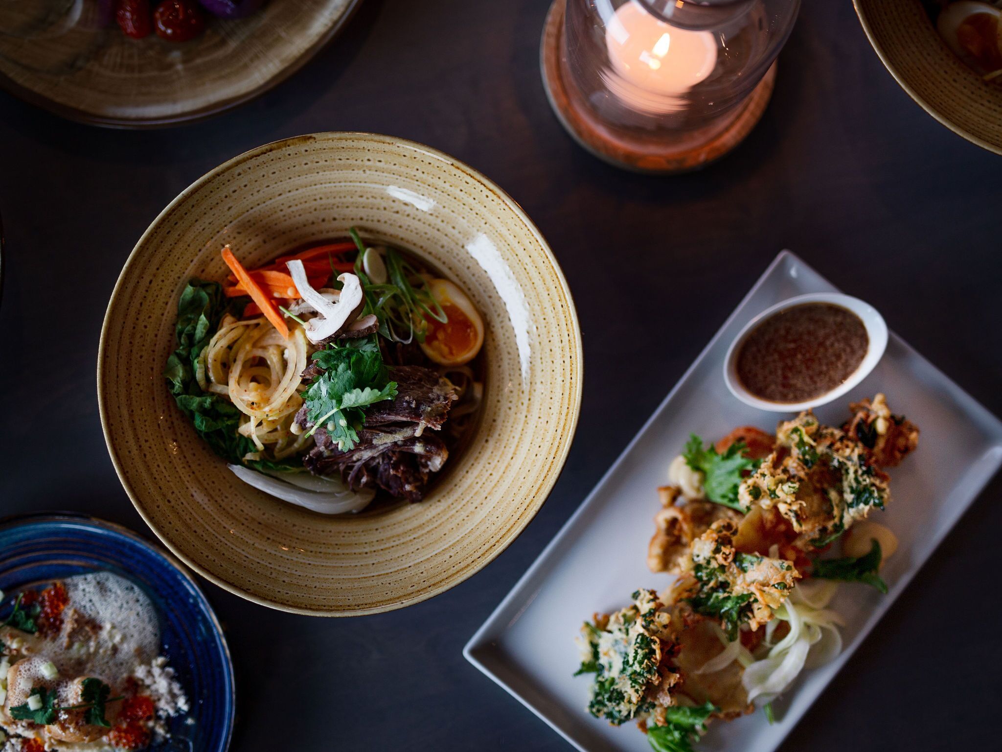 A dining table with a bowl of salad, a plate of crispy vegetables, and a candle.