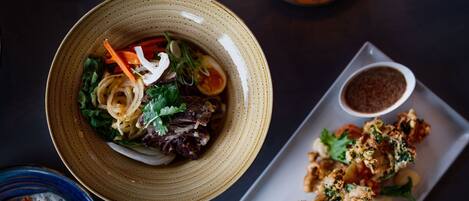 A dining table with a bowl of salad, a plate of crispy vegetables, and a candle.