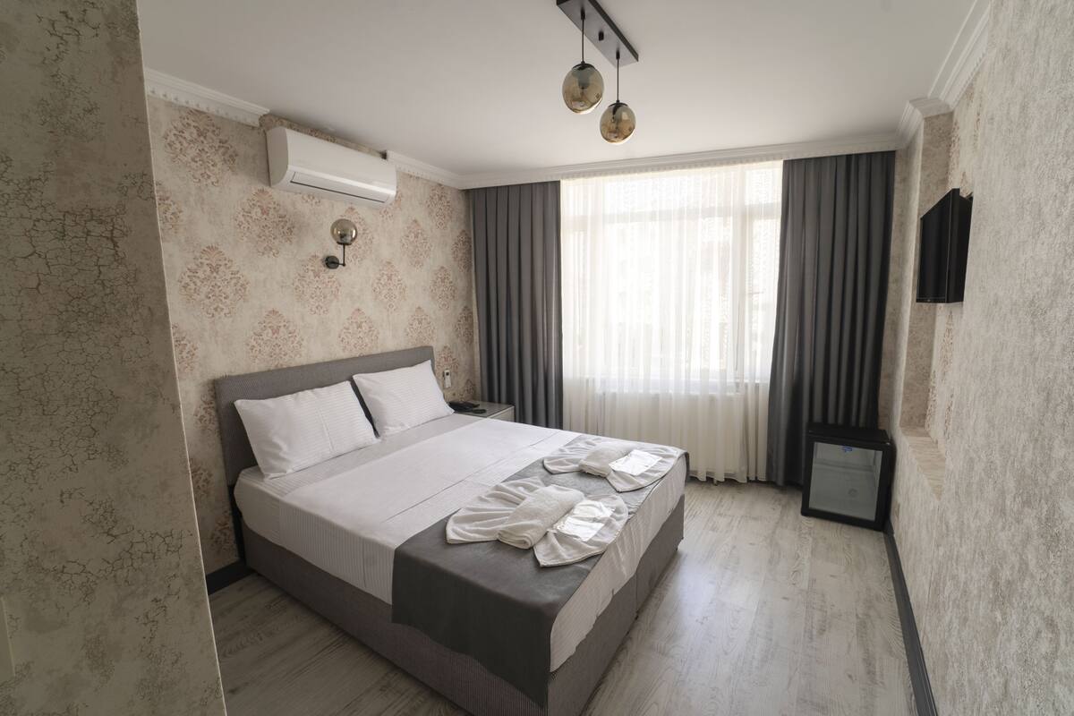 A hotel room with a large bed, a bedside table, a TV, and a window with curtains.
