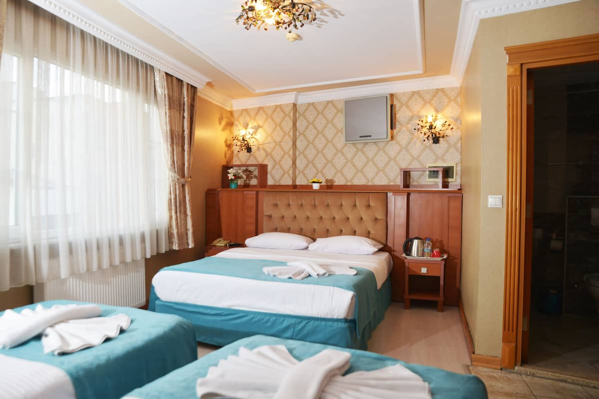 A hotel room with two beds, a wooden headboard, a bedside table with a lamp, and a shower area.
