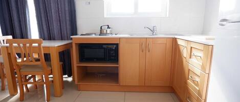 A compact kitchen with a microwave, a kettle, and wooden cabinets.