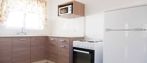 A kitchen with wooden cabinets, a microwave, a stove, and a refrigerator.