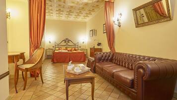 A hotel room with a bed, a leather sofa, a wooden table, a chair, and a mirror on the wall.