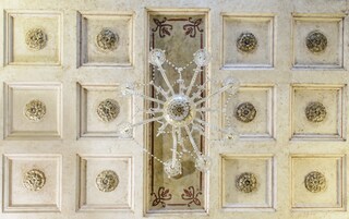 A ceiling with a central chandelier and decorative panels.