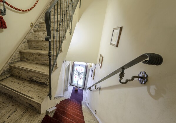 A staircase with a red carpet, a metal railing, and a wall-mounted light fixture.