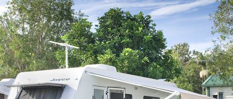 A Jayco RV parked in a grassy area with a covered dining area and a table where two people are seated.