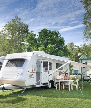 A Jayco RV parked in a grassy area with a covered dining area and a table where two people are seated.