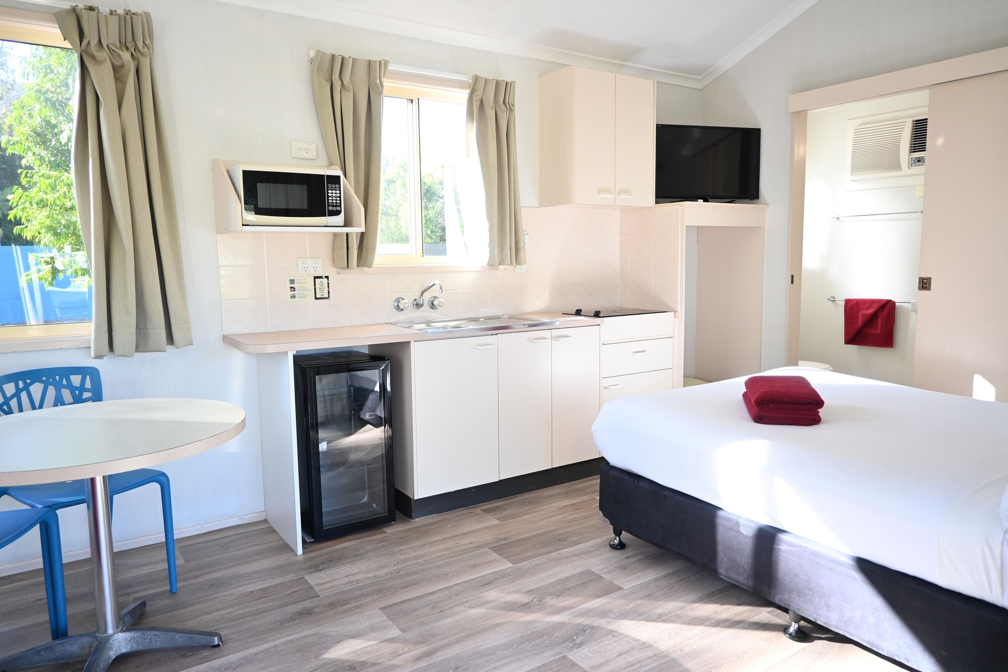 A compact room with a bed, a small kitchenette, a microwave, a TV, and a window with curtains.