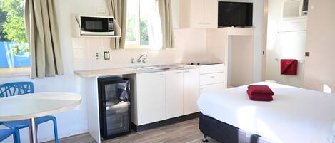 Une chambre de taille modeste comprenant un lit, une petite kitchenette, un four à micro-ondes, une télévision et une fenêtre avec des rideaux.