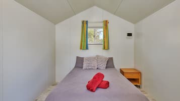 A bedroom with a bed, a window with curtains, a bedside table, and a wall-mounted thermostat.