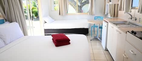 A hotel room with two beds, a kitchenette, and a view of the outdoors.