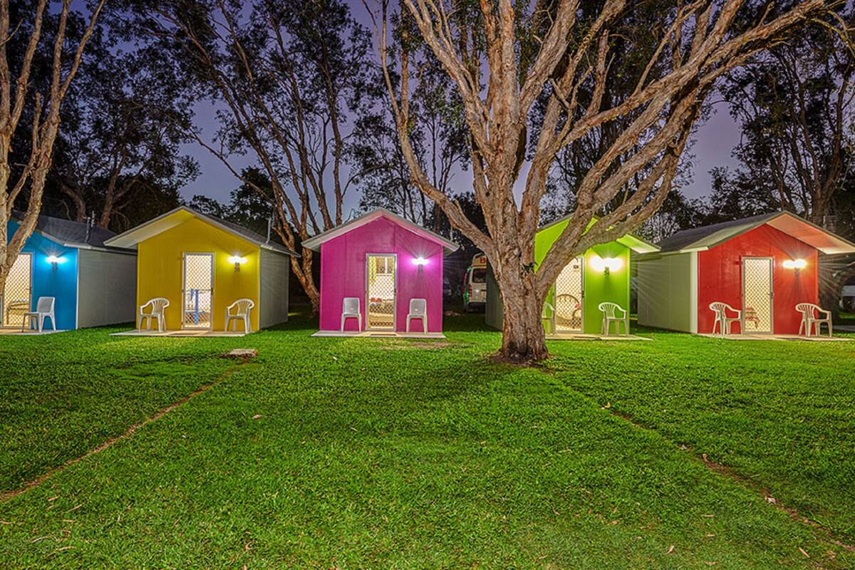 A row of brightly colored cabins with outdoor seating, surrounded by trees and a well-maintained lawn.