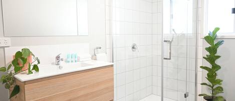 A modern bathroom with a white sink, wooden vanity, and a glass-enclosed shower.