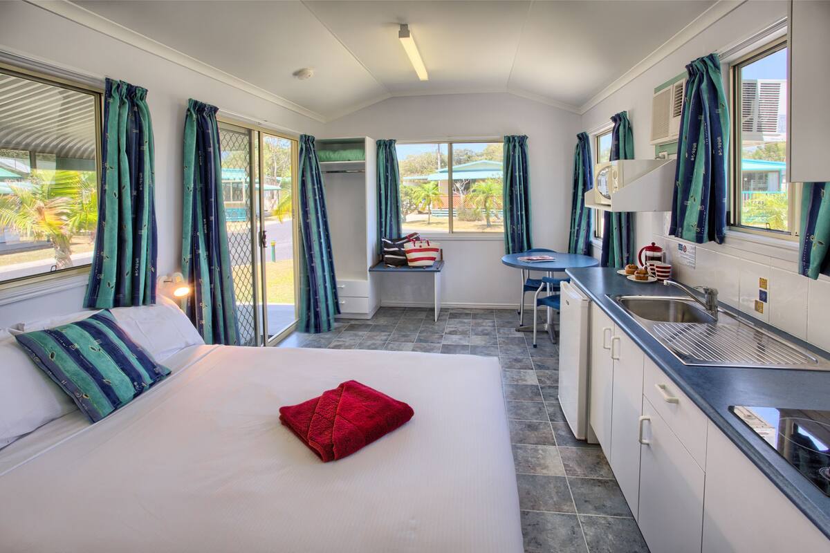 A compact hotel room with a bed, a small kitchenette, and a view of the outdoors.