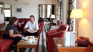 A hotel lobby with red leather sofas, a coffee table with tea and pastries, and a lamp.